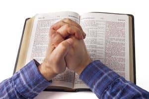 Praying hands over open bible